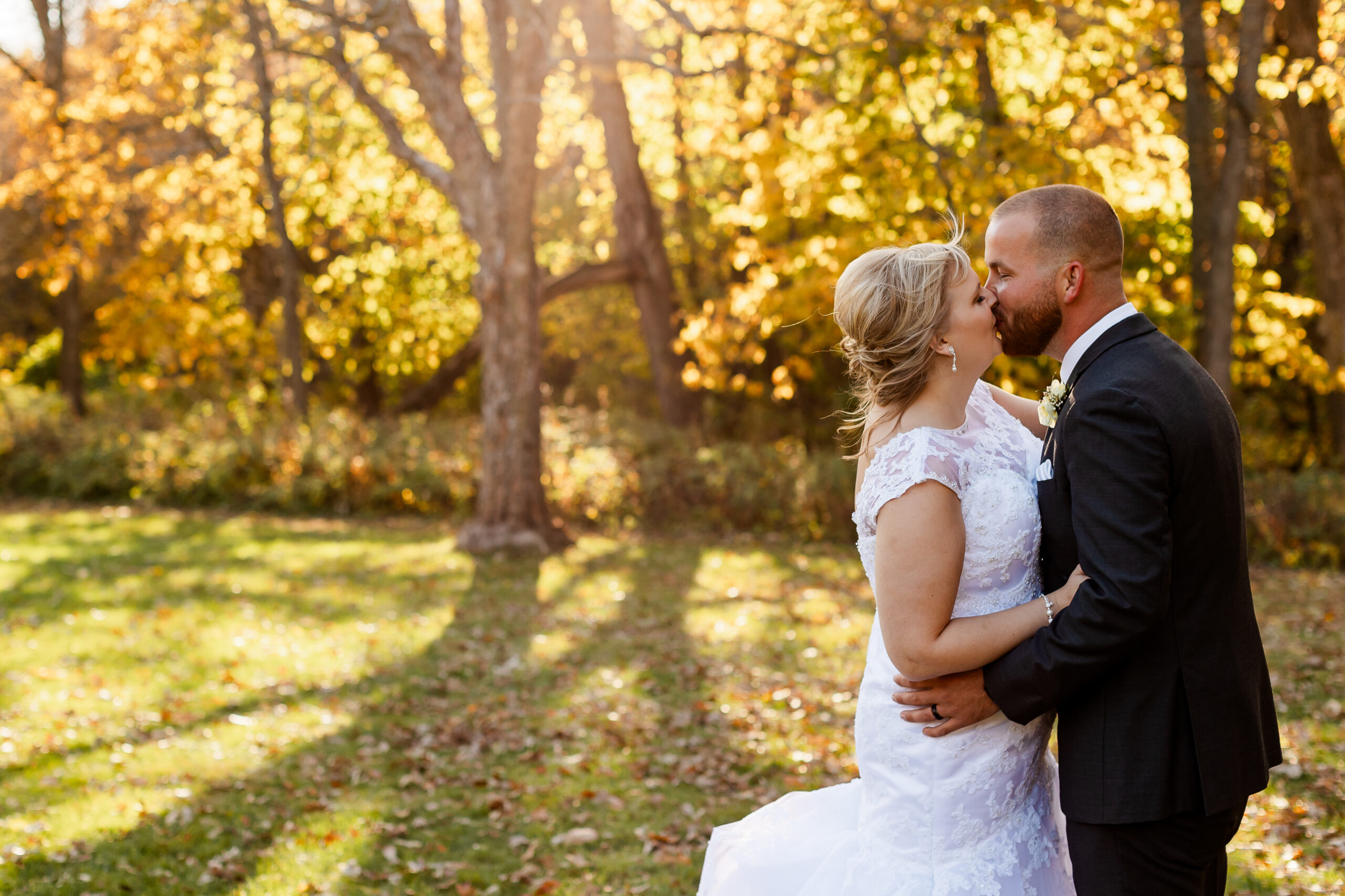 Bride and Groom kiss in front of colorful fall trees at New Wine Park.